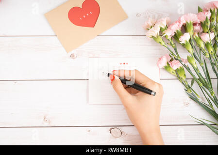 Femme de lettre d'amour écrit sur du papier blanc avec chiffres en forme de coeur rouge.fabriqué à la main en carte postale pour Saint Valentines Day celebration.Envoyer des lettres pour votre lov Banque D'Images