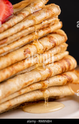 Miel ou sirop d'érable verser sur les crêpes. Vue rapprochée de la pile de fines crêpes, blinis ou des crêpes avec du miel Banque D'Images