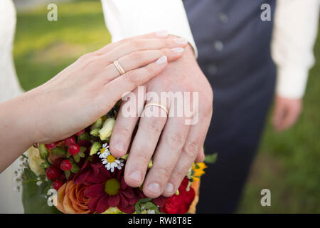 Mains de jeunes mariés avec des anneaux de mariage et bouquet de fleurs Banque D'Images