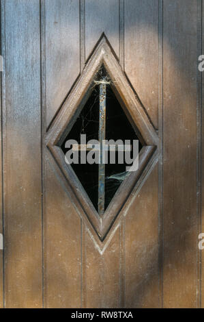 Gros plan d'une fenêtre dans une porte en bois d'une ancienne chapelle routière près de La Roche-en-Ardenne en Belgique. Dans la fenêtre il y a une vieille croix de fer rouillée wi Banque D'Images