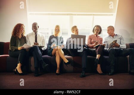 Smiling group de divers hommes d'affaires et assis dans une rangée sur un canapé dans un bureau de travail discussion Banque D'Images
