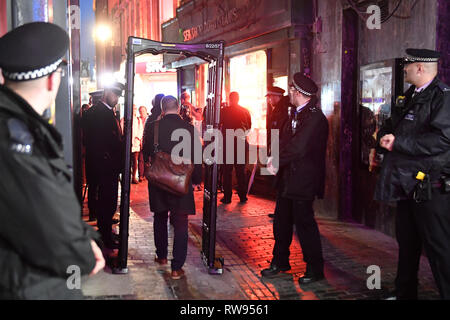 Un homme passe par un passage de couteau qui a été mis en place par les agents de la police métropolitaine de Walker's Court, entre Piccadilly Circus et les stations de métro d'Oxford Circus à Londres. Banque D'Images