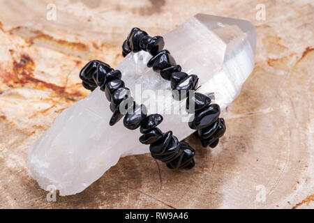 Bracelet Tourmaline Noire enroulée autour de l'arc-en-ciel de Lemurian point quartz du Brésil sur dalle bois pétrifié poli naturel de Madagascar. Banque D'Images