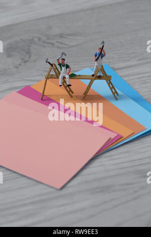 Peinture de couleur swatch cards avec modèle à l'échelle miniature peintres et décorateurs sur un fond en bois gris avec des roses oranges et bleus Banque D'Images