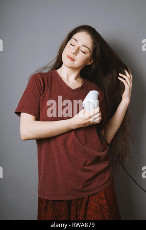 Young woman brushing ses longs cheveux avec un sèche-cheveux Banque D'Images