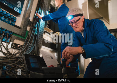 Les électriciens sont la réparation d'un standard téléphonique dans un sous-sol. Banque D'Images