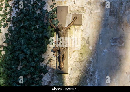 Belle rusty Jésus Christ crucifixion statue pendant le coucher du soleil en partie couverte de lierre, Hedera helix sur vieux mur, cimetière Olsany, Prague, République Tchèque Banque D'Images