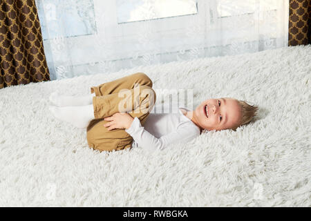 Enfant funny home. Heureux petit garçon blond allongé sur le doux lit couvre-lit, vue du dessus. Petit enfant de rire en regardant la caméra. Banque D'Images