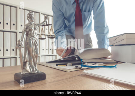 Procureur flipping book pages dans law office, selective focus on statue de Dame Justice avec effet de flou de mouvement Banque D'Images