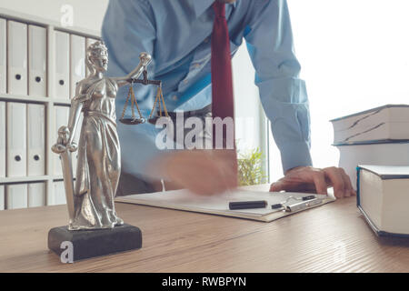 Procureur lecture livre et écrit des notes dans law office, selective focus on statue de Dame Justice, d'une exposition longue, effet de flou de mouvement Banque D'Images