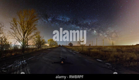 Le mec se trouvant en dessous de la nuit ciel étoilé. Homme étendu sur route asphaltée et voir dans le ciel nocturne. Regarder la voie lactée. Banque D'Images