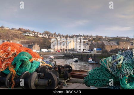 Filets colorés et d'autres équipements de pêche empilés sur le quai à Gourdon, un village sur la côte de l'Aberdeenshire Banque D'Images