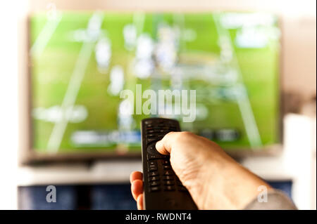 Main tenant une télécommande devant l'écran Banque D'Images