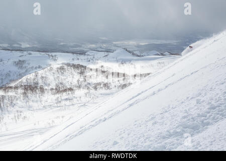 Un skieur de télémark avec veste rouge et son sac à dos se transforme en poudre profonde dans l'arrière-pays près de Niseko Mountain. Banque D'Images