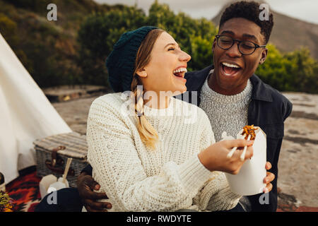 L'Interracial couple outdoors on picnic. Alimentation Alimentation femme à son petit ami alors qu'il était assis à l'extérieur. Banque D'Images