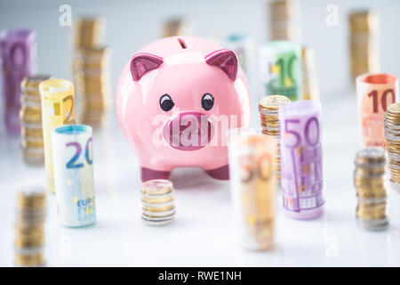 Pink piggy bank au milieu de billets et tours avec des pièces de monnaie Banque D'Images