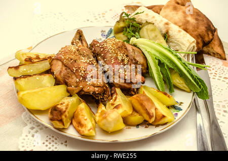 Une grande assiette avec des morceaux de poulet et les pommes de terre, parsemé de sésame blanc et poivre noir, à côté de la salade et le poivre se situent sur une pap blanc Banque D'Images
