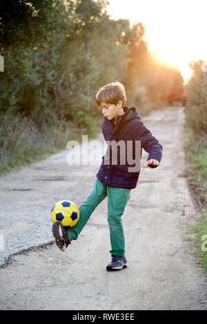 Jeune garçon s'amusant à jouer au football au coucher du soleil Banque D'Images