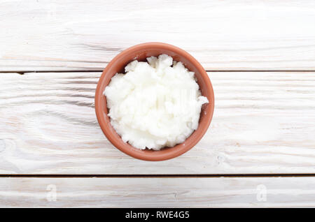 L'huile de noix de coco dans un bol d'argile brun sur table de cuisine en bois blanc Banque D'Images