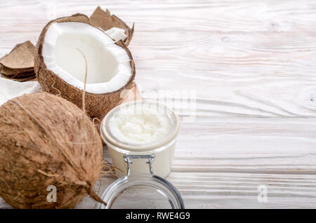 L'huile de noix de coco dans un bocal en verre hermétique et les plaques sur la table en bois blanc libre Banque D'Images