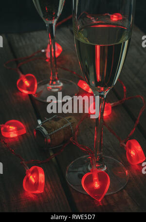 Valentines Day Champagne, deux verres de champagne avec coeur fairy lights autour, sur un fond de bois. L'accent est sur la face avant du verre de champagne. Banque D'Images