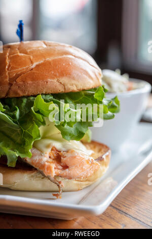 Saumon grillé sur un petit pain grillé avec laitue et fromage, servi avec un petit bol de salade de choux Banque D'Images