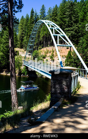 Un bateau ponton va sous le pont piétonnier sur wagon Creek Lake Siskiyou près de Mt. Shasta, Californie, USA. Banque D'Images