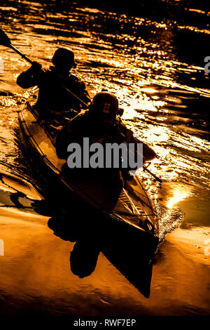 Silhouette d'hommes des forces spéciales de l'Armée de pagaie kayak sur la rivière au crépuscule. Banque D'Images