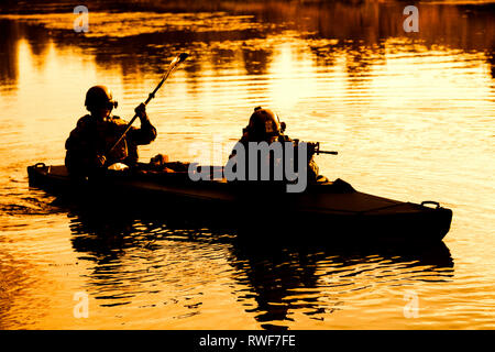 Silhouette d'hommes des forces spéciales de l'Armée de pagaie kayak sur la rivière au crépuscule. Banque D'Images