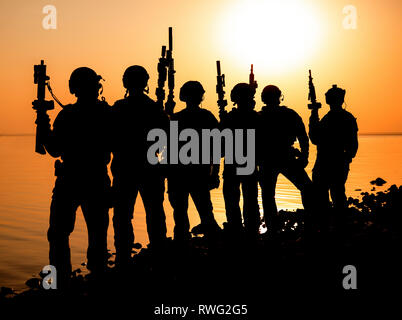 Silhouette d'armée soldats avec des fusils contre une orange au coucher du soleil.