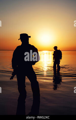 Les soldats de l'Armée de Silhouette traversant une rivière contre un coucher de soleil orange. Banque D'Images