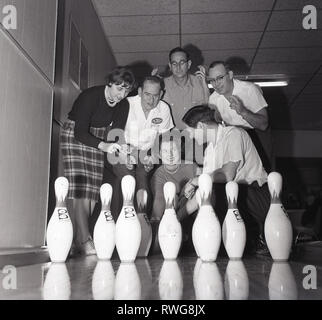Années 1960, joueurs de bowls historiques, masculins et féminins croisant les doigts en espérant une salle complète dans une partie de bowling à dix quilles, dans une piste de bowling à Chicago, États-Unis. Banque D'Images