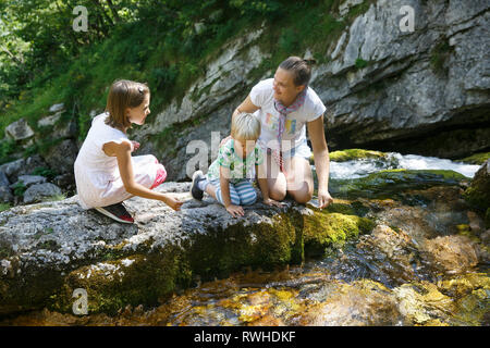 Parler avec les enfants de la mère, de l'eau potable à partir d'un pur, frais et frais ruisseau de montagne sur un voyage en famille. De vie de plein air, les enfants, l'enfance Banque D'Images