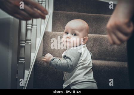 Baby Boy crawling up l'escalier en bois sous les soins de la mère. Banque D'Images