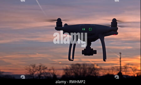 D'un drone en vol stationnaire devant un fond coucher de soleil. Le drone est immobile planant au-dessus du sol que les couchers de soleil au loin. Banque D'Images