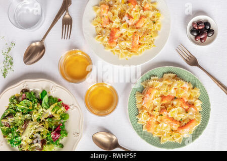 Deux plaques de pâtes au saumon. Farfalle au saumon fumé et à la crème, tourné par le haut avec le vin et les feuilles de salade mesclun Banque D'Images