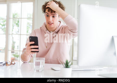 Jeune étudiant man using smartphone et l'ordinateur a souligné avec la main sur la tête, choqué par la honte et la surprise face, en colère et frustrés. La peur et la colère Banque D'Images