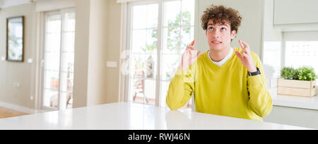 Prise de vue au grand angle de jeune homme séduisant à la maison smiling crossing fingers avec espoir et les yeux fermés. Chance et concept superstitieux. Banque D'Images