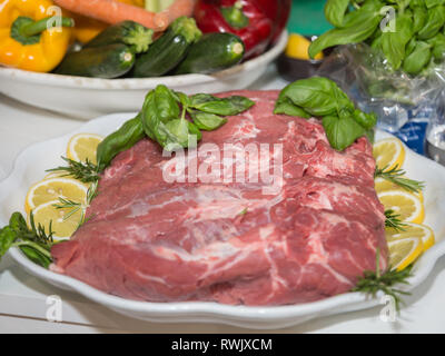 Morceau de boeuf cru sur un plateau garni de tranches de citron et de basilic et de romarin. Banque D'Images