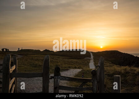 Coucher du soleil d'hiver d'or, l'île Llanddwyn, Anglesey. Vue sur le long chemin du littoral ensoleillé de la péninsule portes de bois en premier plan, naturellement éclairé par un soleil couchant. Banque D'Images