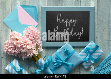 Vert printemps et fond bleu. Tableau avec Jacinthe rose et cadeaux emballés. Mise à plat avec le texte 'Happy Birthday'. Banque D'Images