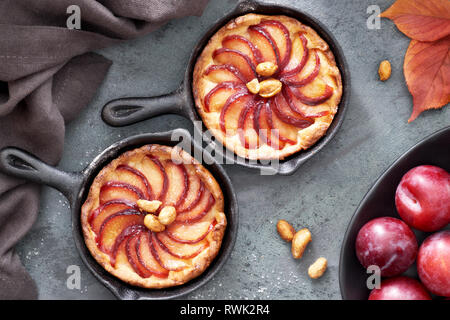 Crumble aux prunes tartes faites maison cuit dans des tranches de petits poêlons en fer. Haut de jeter sur le bord avec un peu de pruneau, noix et feuilles rouges. Banque D'Images