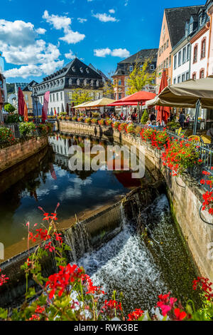 Canal avec chutes d'eau en village coloré avec des jardinières de fleurs le long de rampes et ciel bleu avec des nuages, Saarburg, Allemagne Banque D'Images