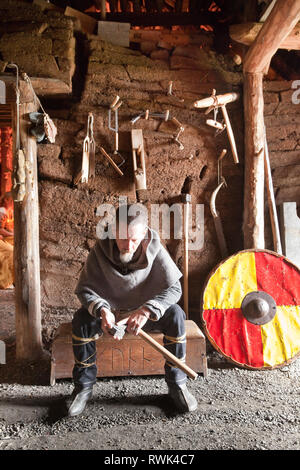 Parcs Canada intepreter en costume d'une hache d'affûtage à l'abri dans une maison longue Viking à L'Anse aux Meadows National Historic Site, L'Anse aux Meadows, Terre-Neuve, Canada Banque D'Images