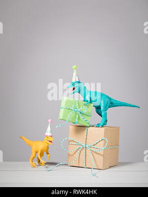 Deux dinosaures avec des chapeaux d'anniversaire et cadeaux sur un fond gris clair. Banque D'Images