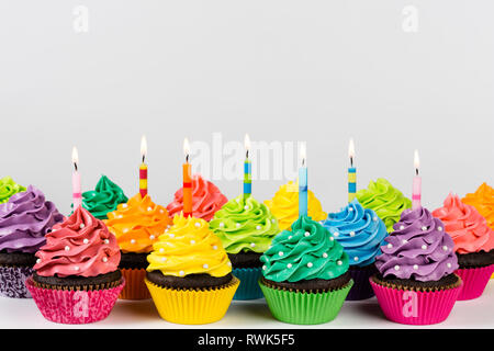 Rangées de cup cakes colorés décorés de bougies d'anniversaire et de paillettes. Banque D'Images