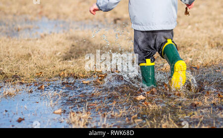 Tout-petit en marche dans les flaques d'eau portant des bottes de pluie. Banque D'Images