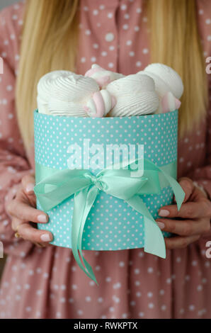 Les mains tenant une grosse boîte turquoise avec ruban rempli de guimauves et de meringues. Banque D'Images
