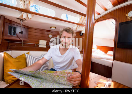 Jeune homme en voilier cabine avec carte pliante, portrait Banque D'Images