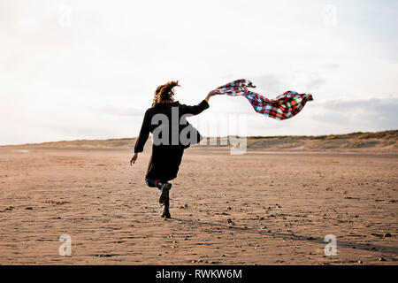 Woman running with beach blanket Banque D'Images